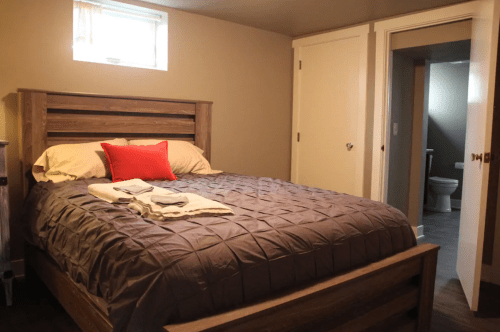 Cozy bedroom with a large bed, gray bedding, and a red pillow, featuring a door leading to a bathroom.