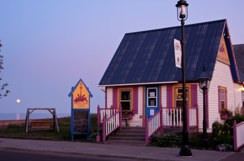 A colorful seaside house at dusk, with a full moon rising in the background and flowers adorning the porch.
