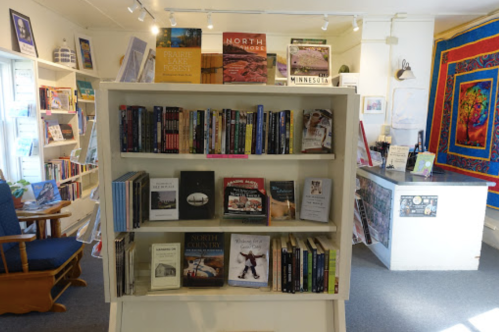 A cozy bookstore interior featuring a bookshelf filled with various books and a colorful quilt on the wall.