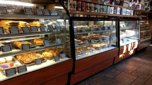 A display case filled with various baked goods, including pastries, muffins, and desserts, in a cozy bakery setting.