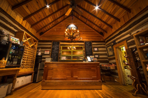 Cozy wooden interior of a rustic reception area with a chandelier and a wine rack. Warm lighting enhances the ambiance.