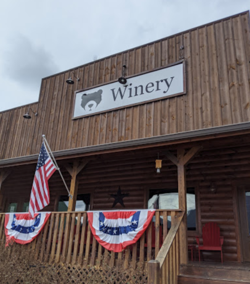 A rustic winery building with a bear sign, American flag, and patriotic decorations on the porch.