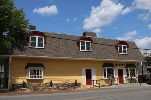 A yellow winery building with a sloped roof, red accents, and a stone foundation under a blue sky with clouds.