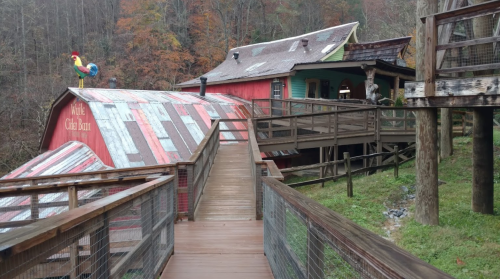 A wooden walkway leads to a colorful barn-style building surrounded by autumn foliage.