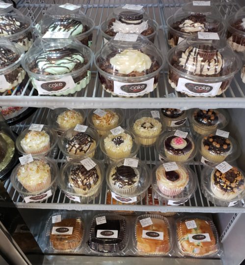 A display case filled with various cupcakes in clear containers, showcasing different flavors and toppings.