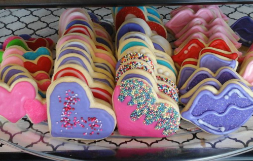 A colorful assortment of heart and lip-shaped cookies, decorated with icing and sprinkles, displayed on a tray.
