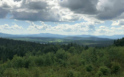 A scenic view of rolling mountains and lush green forests under a partly cloudy sky.