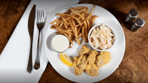 A plate with fried oysters, French fries, coleslaw, a lemon wedge, and a small cup of dipping sauce.