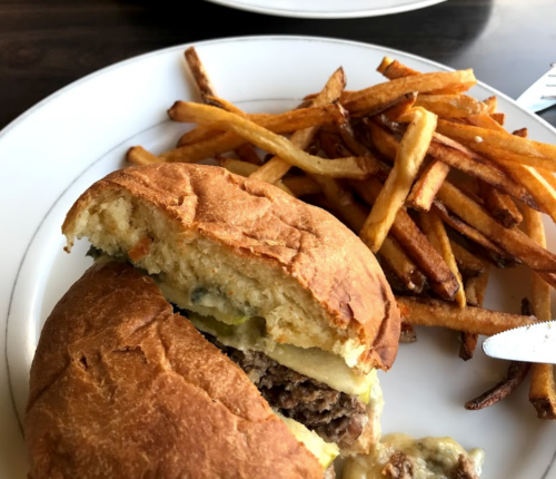 A close-up of a burger with a bite taken out, served with a side of golden, crispy French fries on a white plate.
