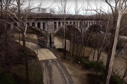 Aerial view of a stone bridge over a river, surrounded by bare trees and a winding road.