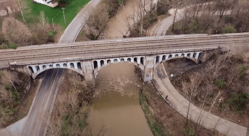 Aerial view of a railway bridge over a river, surrounded by trees and roads.