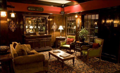 Cozy interior with wooden walls, a mirror, vintage furniture, and a plant, creating a warm, inviting atmosphere.