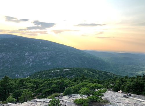 A scenic view of rolling hills and valleys under a sunset sky, with lush greenery in the foreground.