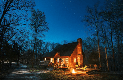 A cozy cabin in the woods at night, illuminated by stars and a warm fire, surrounded by trees.