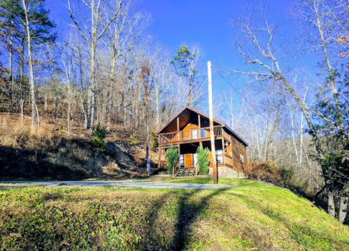 A cozy wooden cabin on a hillside, surrounded by bare trees and a clear blue sky.
