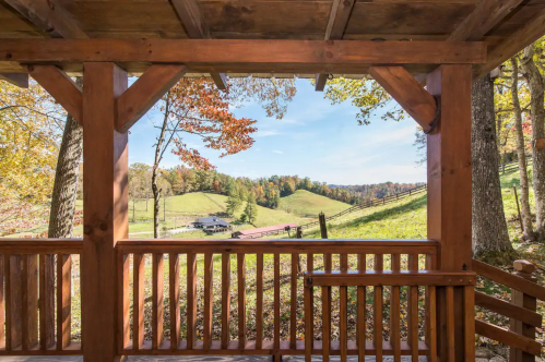 View from a wooden porch overlooking rolling green hills and colorful autumn trees under a clear blue sky.