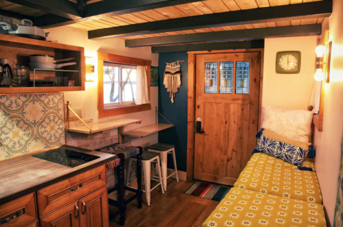 Cozy kitchen and living area with wooden accents, a door, and a bright yellow daybed against a blue wall.