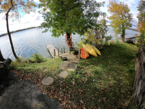 A serene lakeside scene with a wooden dock, colorful kayaks, and autumn foliage reflecting on the water.
