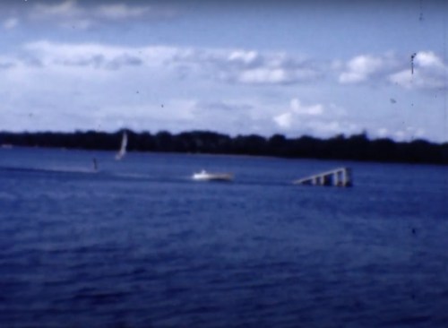 A blurred image of a lake with a small boat and a dock, under a blue sky with scattered clouds.