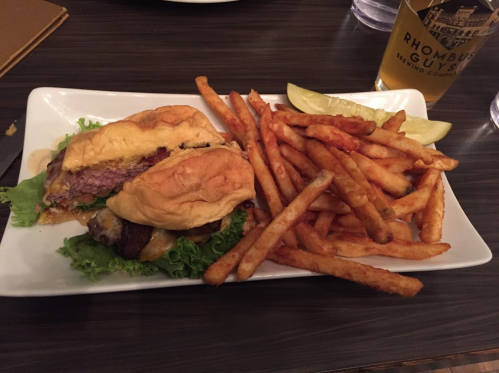A plate with a burger topped with lettuce and cheese, accompanied by a side of crispy fries and a lemon wedge.