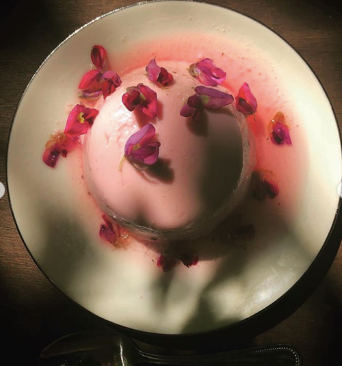 A creamy pink dessert topped with edible flowers, served in a shallow bowl with a hint of sauce around it.
