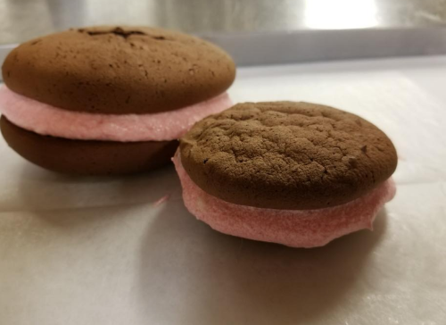 Two chocolate whoopie pies with pink filling, resting on a white surface.