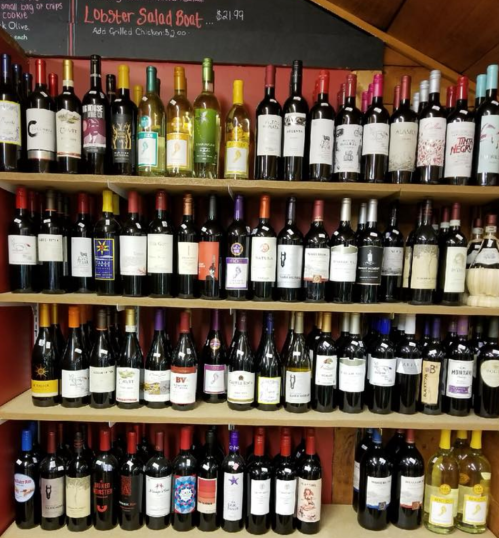 A wooden shelf displaying a variety of wine bottles with colorful labels, organized in rows.