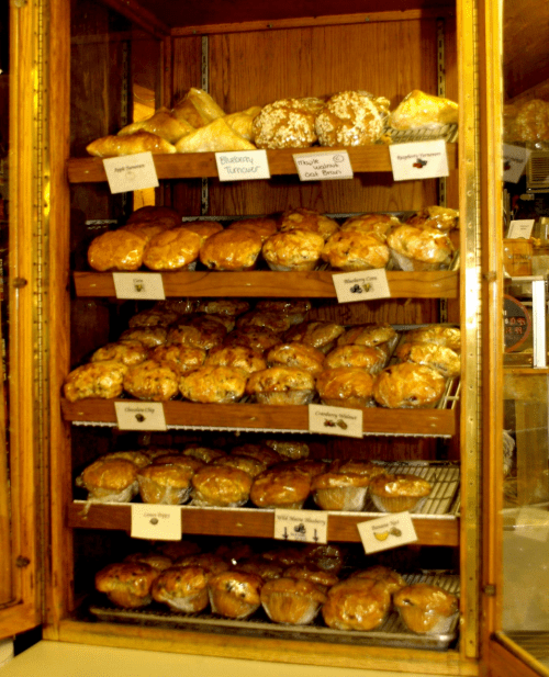 A display case filled with various baked goods, including muffins and pastries, arranged on wooden shelves.