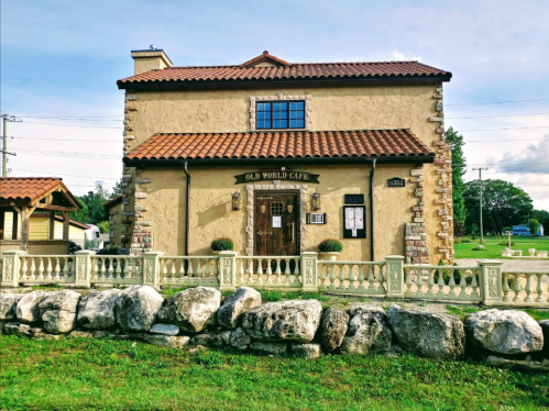 A charming café with a stone exterior and tiled roof, surrounded by a grassy area and decorative stone wall.