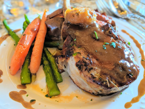 A plated meal featuring a pork chop with gravy, asparagus, carrots, and a side of potatoes.