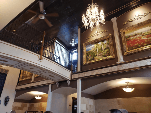 Interior of a stylish restaurant featuring a chandelier, artwork on the walls, and a second-floor balcony.