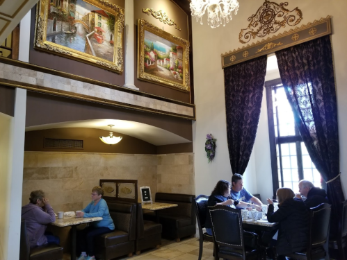 A cozy café interior with paintings, elegant decor, and patrons enjoying their meals at tables and booths.