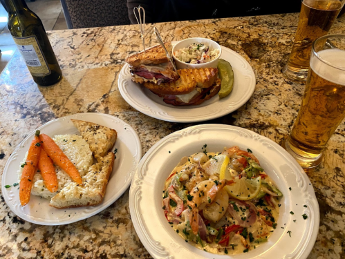 A table with two plates: one with shrimp and vegetables, the other with a sandwich, coleslaw, and pickles, plus drinks.
