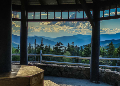A scenic view from a gazebo overlooking mountains and trees under a cloudy sky.