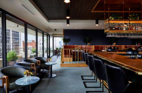 Stylish bar interior with modern seating, large windows, and a well-stocked bar overlooking a cityscape.