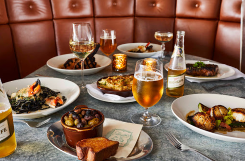 A table set with various gourmet dishes, glasses of wine, and beer, surrounded by warm candlelight.