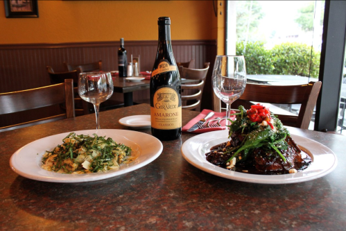 A table setting with two plates of food: one with pasta and greens, the other with a meat dish, and a bottle of wine.