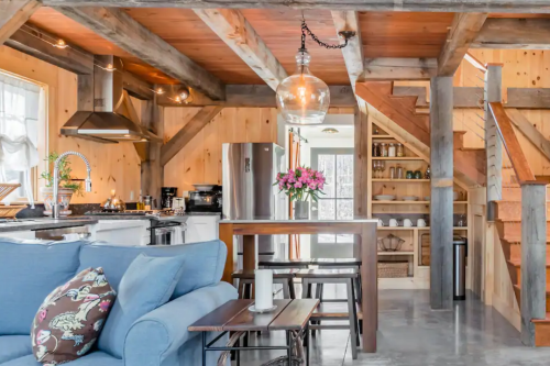 Cozy wooden cabin interior featuring a kitchen, dining area, and staircase with natural light and floral decor.