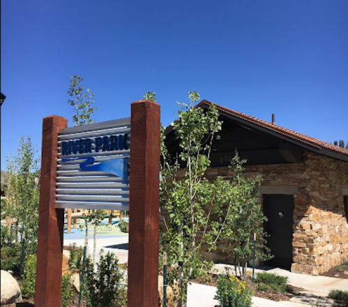 Sign for a water park with a stone building and greenery under a clear blue sky.