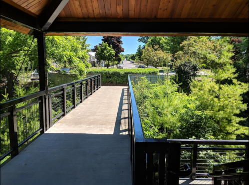 View from a covered deck overlooking a pathway and lush greenery on a sunny day.