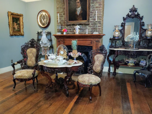 A vintage room featuring ornate furniture, a wooden fireplace, and decorative art pieces on the walls and tables.