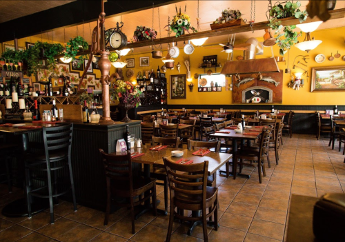 Cozy restaurant interior with wooden tables, chairs, and vibrant yellow walls adorned with decor and plants.