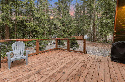 A wooden deck surrounded by tall trees, with a chair and a view of a serene forest at sunset.