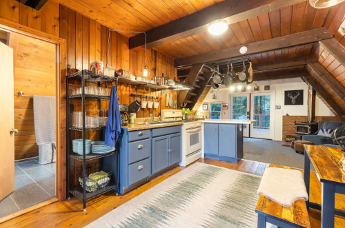 Cozy kitchen with wooden walls, blue cabinets, and an open layout, featuring a dining table and living area in the background.