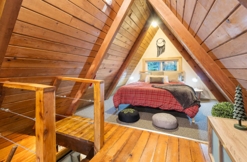 Cozy A-frame bedroom with wooden walls, a plaid blanket, and a view of nature through a large window.