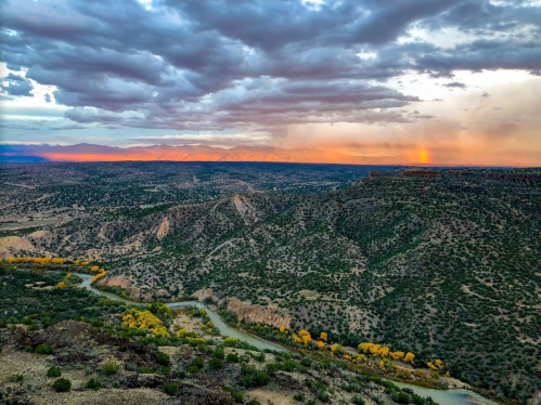 A panoramic view of a rugged landscape with rolling hills, a winding river, and a colorful sunset sky.