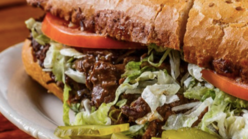 A close-up of a hearty sandwich filled with lettuce, tomato, and savory beef, served on a toasted bun.