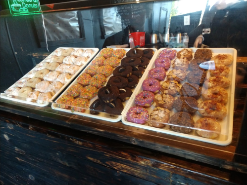 A display case filled with various colorful donuts, including glazed, chocolate, and sprinkled varieties.