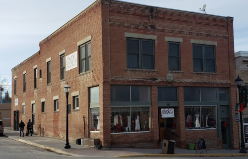 A brick building with large windows, featuring a clothing store display and a couple walking nearby.