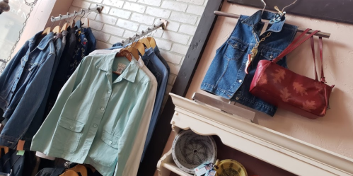 A display of various jackets and a red handbag hanging on racks against a light brick wall.